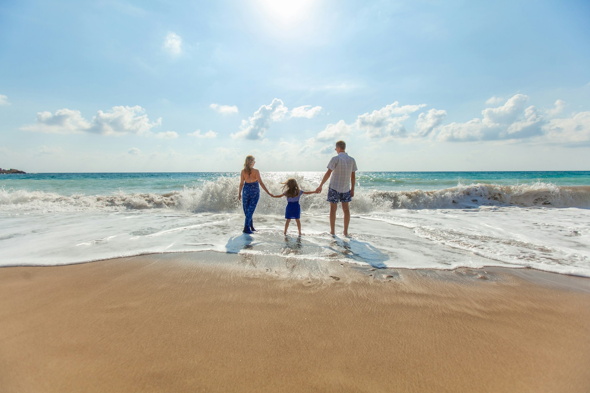 A family of three holding hands at the edge of the surf on a Cyprus beach