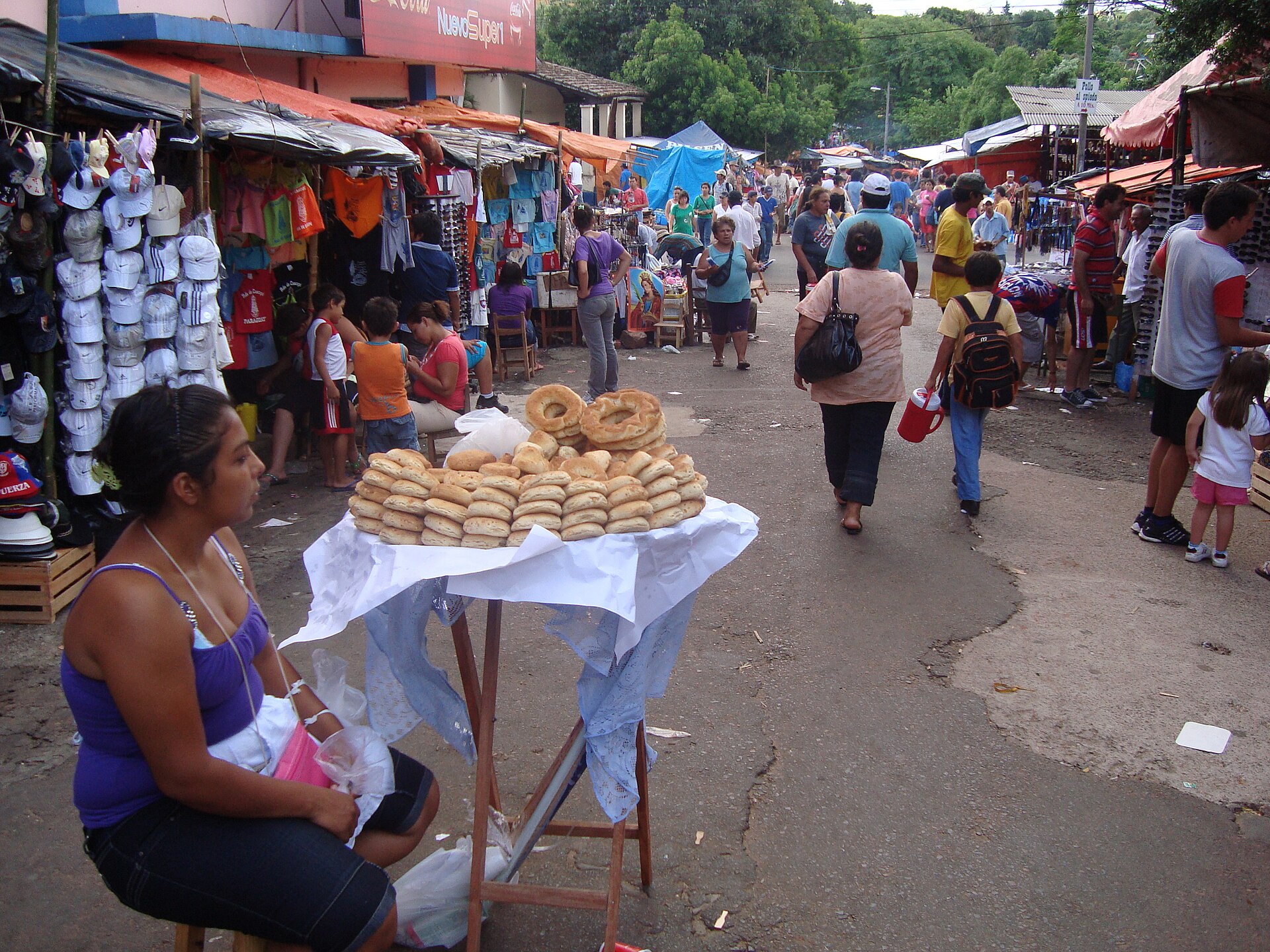A chipa seller at her stall on a crowded market street in Caacupé, Paraguay