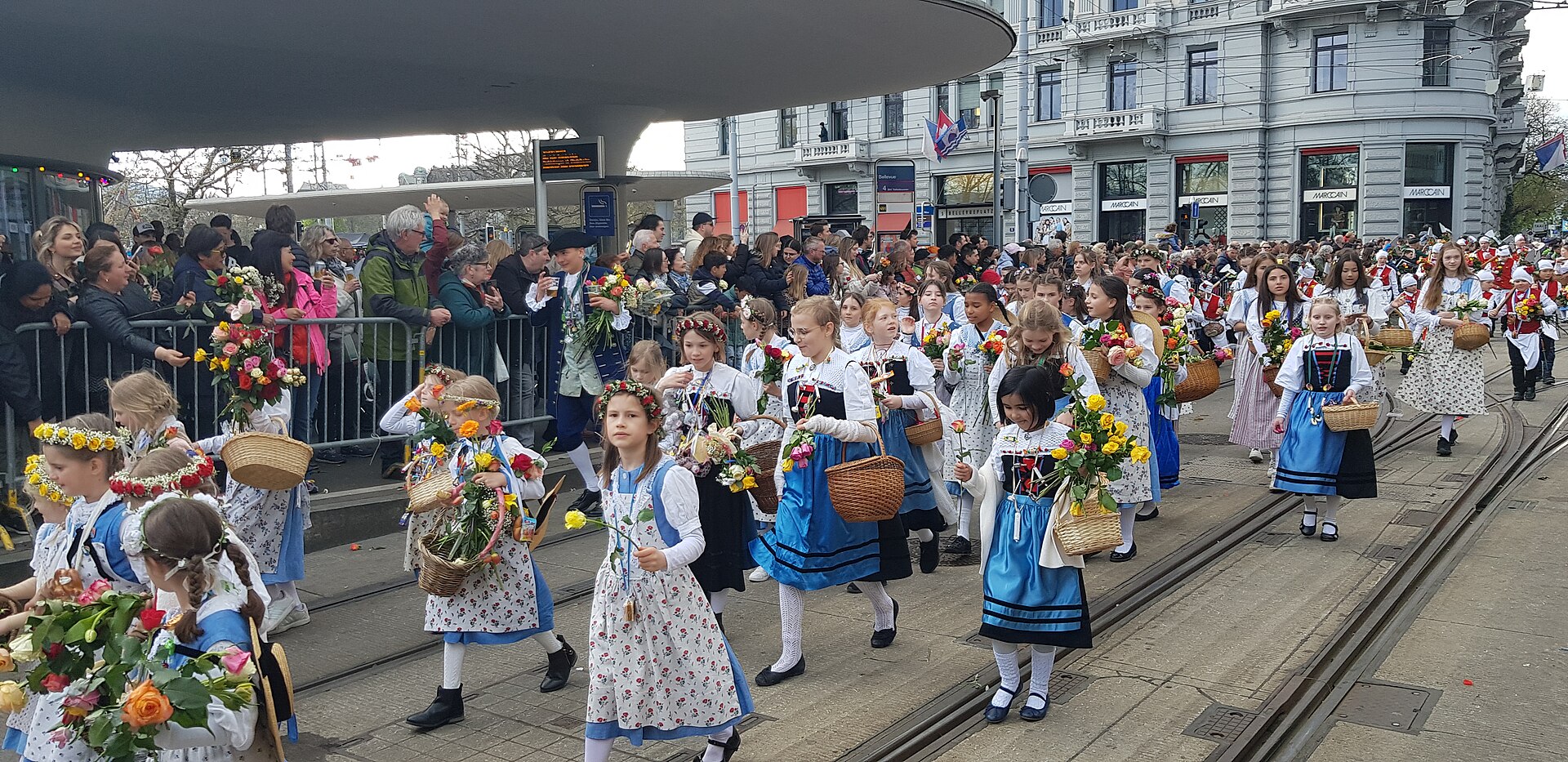 Crowds line a Zurich street as children in traditional dress walk past during the Sechselauten parade
