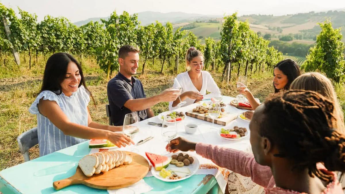 Friends sharing a long dinner at a vineyard table at sunset
