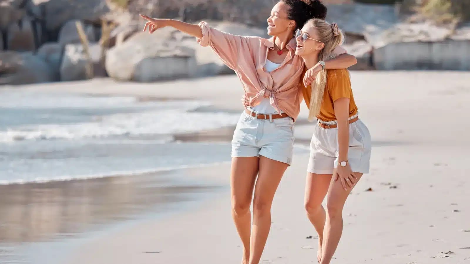 Two women walking along an Australian beach, one pointing out to sea